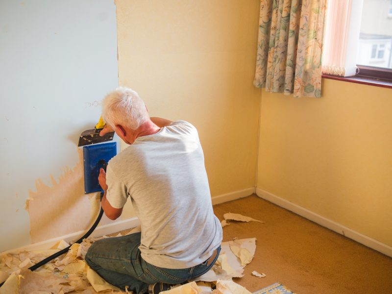 a man removes old wallpaper from a wall using special equipment