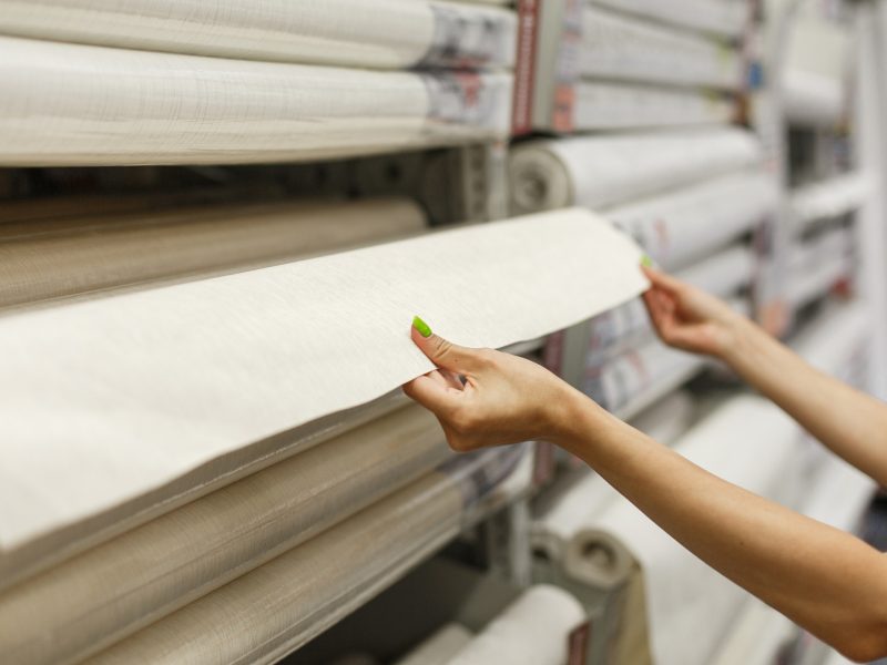 A young woman in a hardware store buys wallpaper. Pulls a roll of wallpaper from the shelf.