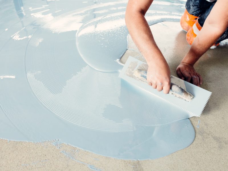 Construction worker spreading self-leveling concrete on the floor using a trowel