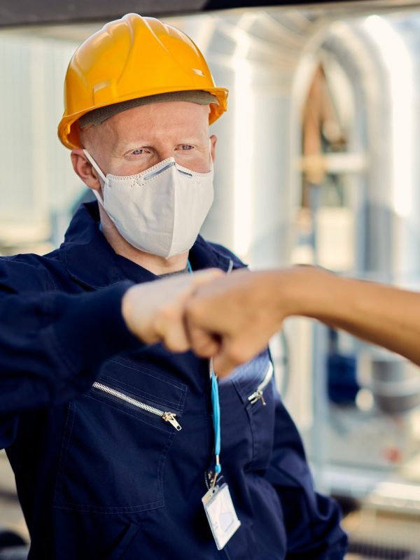 Construction workers with face masks fist bumping during coronavirus epidemic.