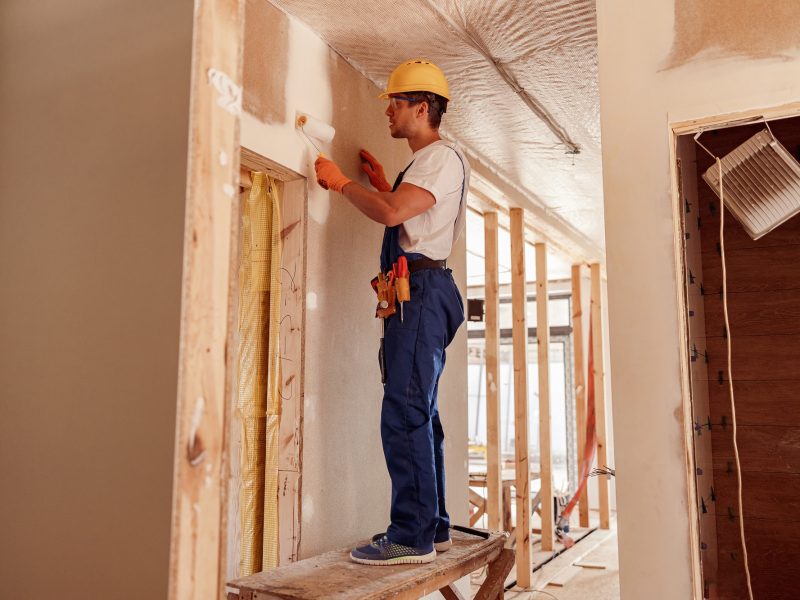 Male builder painting wall in house under construction