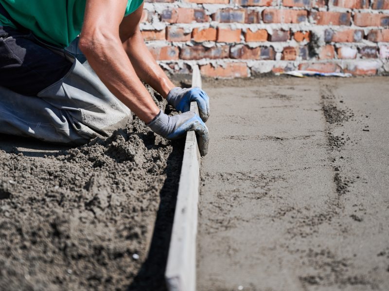 Male builder screeding floor at construction site.