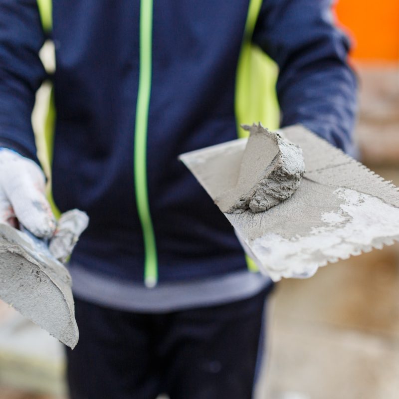 The builder holds in his hands two construction spatulas with plaster